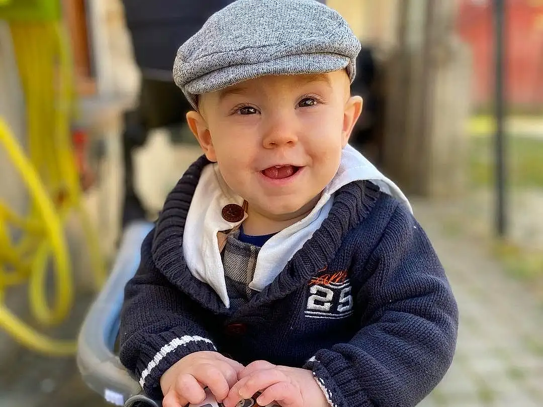 Yeux, Sourire, Plante, Cap, Flash Photography, Jacket, Happy, Street Fashion, Bambin, Chapi Chapo, Baby Carriage, Herbe, Recreation, Assis, Personal Protective Equipment, Baby Products, Camera, Automotive Wheel System, Fun, Beanie, Personne, Headwear