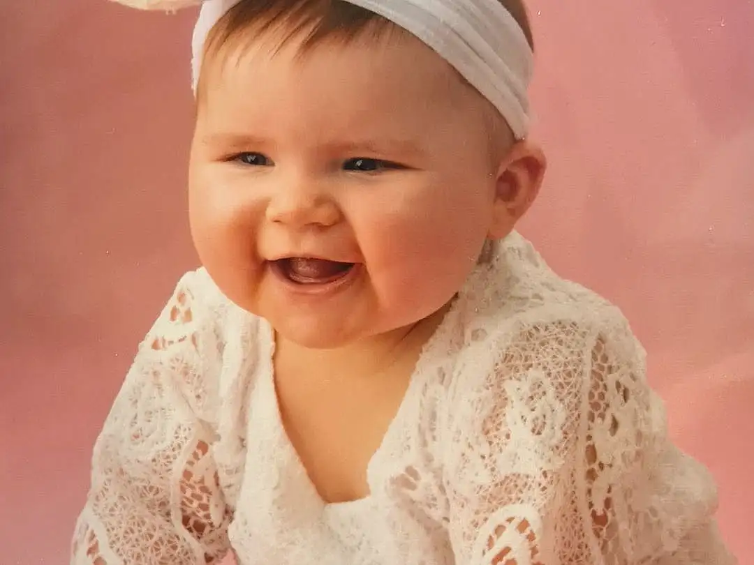 Visage, Peau, Sourire, Head, Chin, Facial Expression, Baby & Toddler Clothing, Sleeve, Dress, Rose, Happy, Baby, Bambin, Enfant, Pattern, Fun, Assis, Fashion Accessory, Peach, Flash Photography, Personne